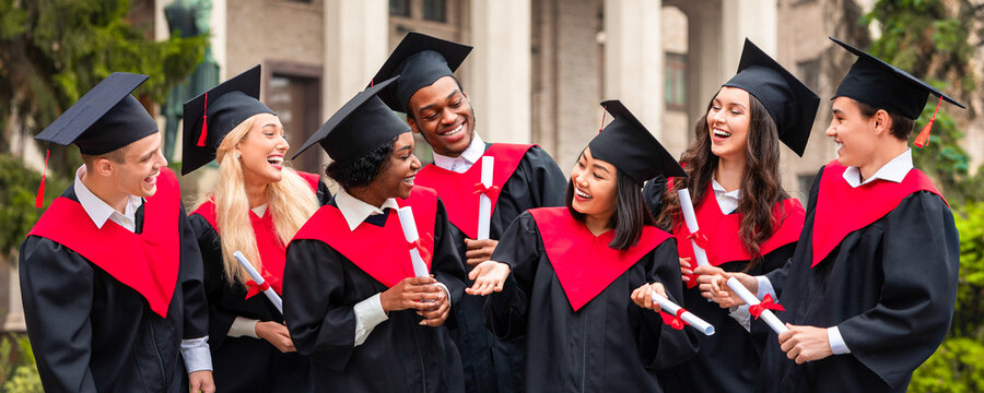 Fototapeta Happy graduates international group of young men and women in graduation costumes holding diplomas, looking at each other and chatting, having ceremony, university campus background
