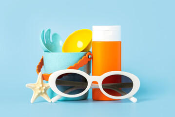Closeup of bottle of sunscreen, white sunglasses and beach bucket. Concept of sun protection and summer