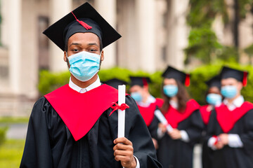 Black guy student in graduation costume showing diploma at camera, posing over international group...