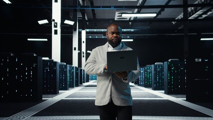 Fototapeta premium Data center system administrator coding on laptop, doing software updates. Server room IT specialist looking at device screen, optimizing infrastructure rackmounts configuration rigs, camera A