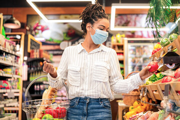 Grocery Shopping. Black Woman Choosing Fresh Vegetables In Supermarket, Walking With Basket Full Of Food Along Shelves In Store Aisle. Groceries Shop Sales And Discounts Concept