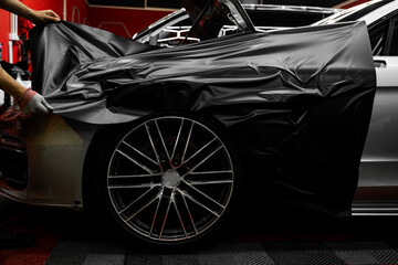 Matte black vinyl is applied across car hood. Car wrapping process using black matte vinyl...
