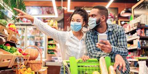 Family At Supermarket. Black Couple With Phone Doing Grocery Shopping Together Walking With Cart...