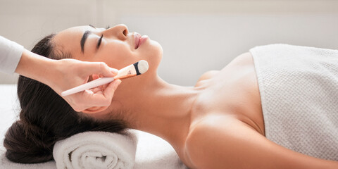 Relaxed asian woman enjoying beauty treatments in spa centre, waiting for beautician to apply facial clay mask, having wellness day at parlor, lying on massage table with closed eyes, side view