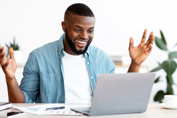 Fototapeta na wymiar Happy Black Freelancer Man Celebrating Success While Working Online On Computer, African Guy Looking At Laptop Screen, Raising Hands And Exclaiming With Excitement, Sitting At Desk In Home Office