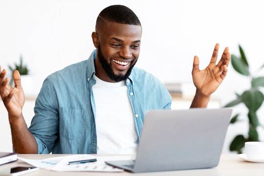 Happy Black Freelancer Man Celebrating Success While Working Online On Computer, African Guy Looking At Laptop Screen, Raising Hands And Exclaiming With Excitement, Sitting At Desk In Home Office