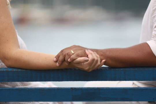 Conex&atilde;o &agrave; beira-mar: um casal de m&atilde;os dadas, sentado em um banco de frente para o mar. A imagem captura a intimidade, o carinho e a tranquilidade de um momento a dois, com o horizonte ao fundo.