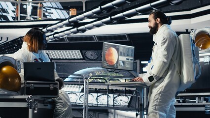 Astronaut monitoring system diagnostics on monitor, talking to colleague during human expansion in...