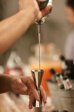 A arte de misturar: um bartender prepara um drink em movimento, com a bebida sendo derramada de uma coqueteleira. A imagem capta a precis&atilde;o e a eleg&acirc;ncia do momento, com um fundo borrado e alegre