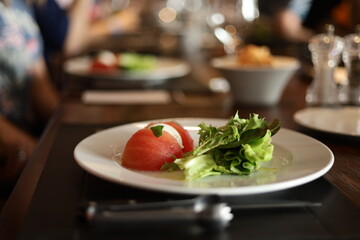 Frescor à mesa: um prato elegante com salada verde e tomate, destacando a simplicidade e o frescor da culinária. A cena, com fundo de restaurante desfocado, sugere uma refeição leve e agradável.