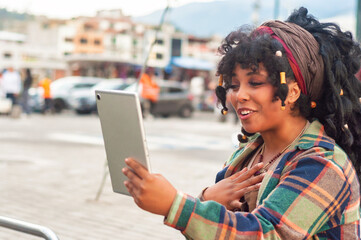 Young latin american woman making a video call with digital tablet in the city