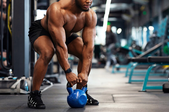 Muscular shirtless african american bodybuilder exercising with kettlebell at gym, looking at copy space. Athletic black man making weightlifting or powerlifting, working on body musculs