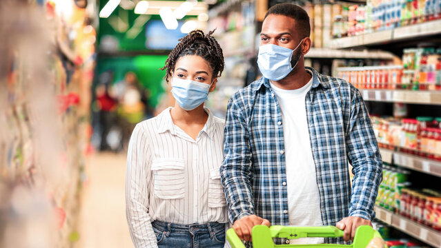 Food Shopping. African American Family Couple In Supermarket Walking Pushing Cart Full Of Healthy Grocery Buying Products In Store, Wearing Protective Face Masks. Consumers In Groceries Shop