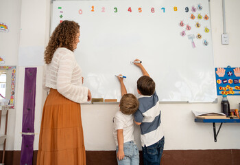 Two young children write on a whiteboard. One stretches to reach higher, illustrating physical growth and height differences in early childhood