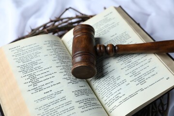 Judge's gavel, crown of thorns and Bible on white fabric, closeup