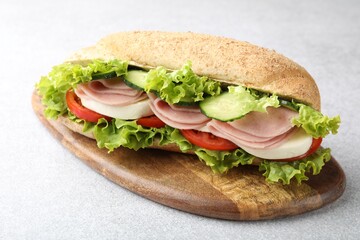 Tasty baguette sandwich with ham and vegetables on light grey table, closeup