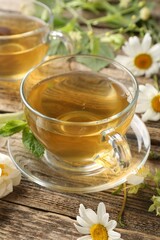 Aromatic herbal tea in glass cups, mint and flowers on wooden table, closeup