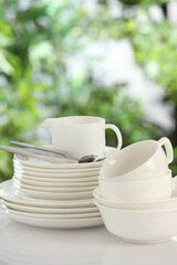 Different clean dishes on white table against blurred green background