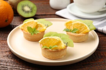 Tartlets with fruits and mint on wooden table, closeup. Delicious dessert