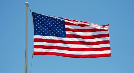 Fototapeta premium Waving American flag against a bright blue sky, emphasizing vibrant colors and dynamic motion.