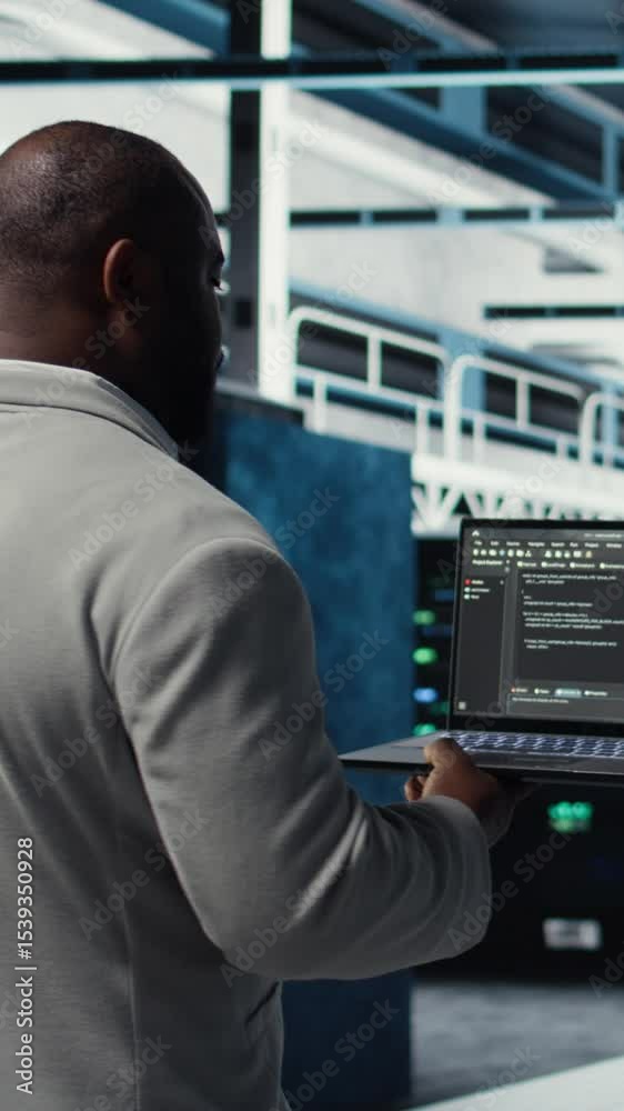 Poster vertical video data center computer scientist coding on laptop, doing software updates. african amer