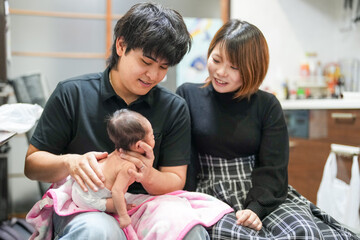 Obraz premium A two-week-old Japanese baby lies wrapped in a pink blanket, held close in the arms of loving parents in their early twenties, quietly drinking milk from a baby bottle in a warm, peaceful moment.