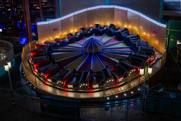 A brightly lit amusement park ride composed of multiple red and black car-shaped seats