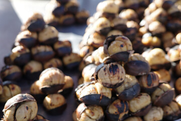 Roasted chestnuts stacked in small piles on a street food stall, with charred shells partially open to reveal the golden nut inside. A warm, rustic, and traditional winter snack scene.