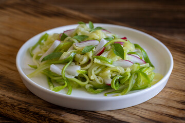 Vegetarian salad with fresh pickled zucchini in spaghetti shape and radish on white plate on wooden table, side view, close up