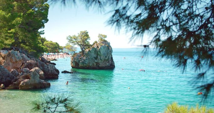 Scenic beach view with clear waters, rocky islet and swimmers in Brela Croatia