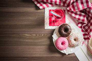 Overhead view of donuts and a drink on a wooden table with a red and white checkered cloth nearby