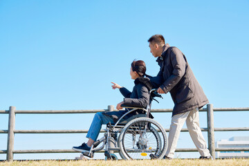 Obraz premium 妻が乗る車椅子を押して散歩する夫