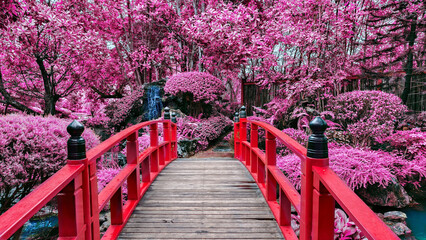 Vibrant red bridge crosses serene stream in garden filled with lush pink foliage, creating dreamlike atmosphere