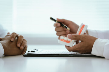 A dentist uses a pen to explain a dental model to a patient, discussing oral health and treatment options.