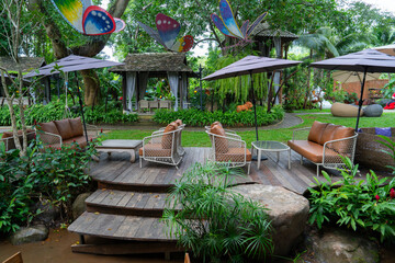 Outdoor seating area with wooden deck, surrounded by lush greenery and colorful butterfly decorations. Relaxing atmosphere