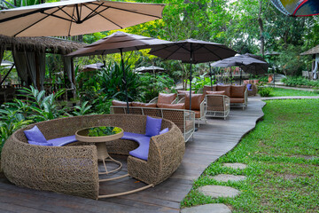 Outdoor seating area with wicker furniture and umbrellas in lush garden setting. Relaxing atmosphere