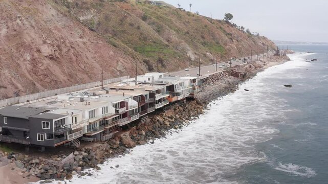 Aerial low close-up shot of surviving beachfront homes alongside cleared lots on Pacific Coast Highway in the aftermath of the Palisades Fire in Malibu, California. 4K