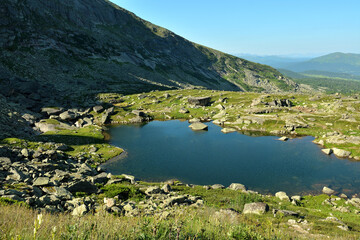 A small picturesque lake with rocks scattered along the banks at the foot of a high cliff on a sunny summer morning.