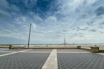Wide, off-season view of Platja de la Patacona promenade near Valencia shows patterned tiled plaza,...
