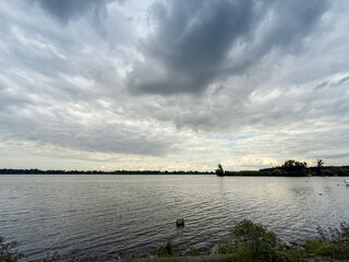 Wide angle view across the Danube at Grocka, a Belgrade suburb in Serbia: calm river surface under brooding summer clouds, low wooded banks and a small island form the distant horizon.