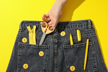 Jeans, tools and hand on yellow background, top view