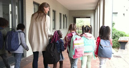 Teacher walking with diverse group of children wearing backpacks at school - Powered by Adobe