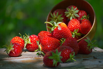 Bright red strawberries spilling from a wooden bowl on a wooden surface.