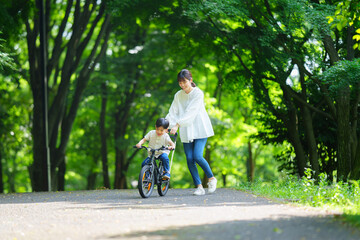 Obraz premium 自転車の練習をする5歳の男の子とフォローする母親