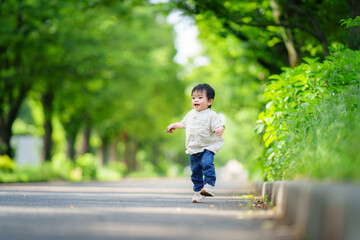 公園の並木道で走る1歳の男の子