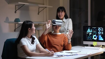 Two young Asian businesswomen are working together in office at night, experiencing virtual reality using a VR headset - Powered by Adobe