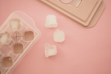 Ice cubes on a pink background with an ice tray