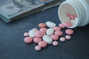 Various pills are spilled from a container next to cash on the table