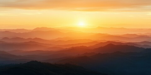Fototapeta premium Scenic view of layered mountain ranges bathed in warm golden light of sunrise with soft mist and vibrant orange sky