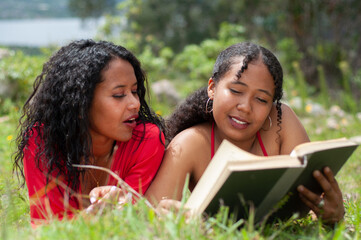 Two latin women reading and enjoying a book together outdoors